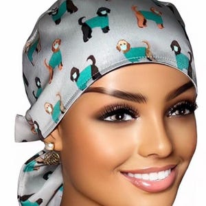 May include: A gray and teal surgical scrub hat with a pattern of dogs wearing surgical masks. The hat has a tie at the back.