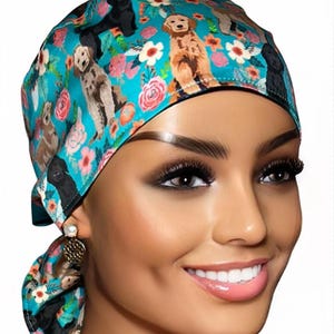 May include: A turquoise blue surgical scrub hat with a pattern of dogs and flowers. The hat has a black trim and a tie at the back.