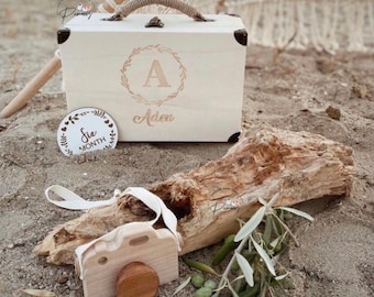 May include: A white wooden box with a handle and a gold inscription that reads "A Aden". The box is sitting on a wooden log with a small wooden camera and a round wooden sign that says "Six Month" on it.