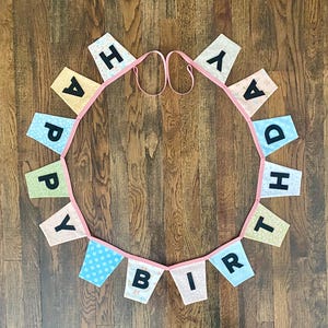 May include: A pink and blue fabric banner with the words "Happy Birthday" in black letters.