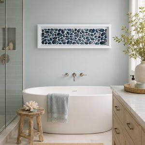 Puede incluir: Una pieza de arte mural rectangular que presenta una colección de formas similares a guijarros en azul oscuro y blanco dispuestas en un patrón de cuadrícula, encerrada en un marco blanco simple y montada horizontalmente sobre una bañera ovalada blanca.