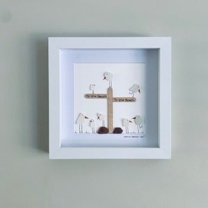 May include: A framed artwork featuring a group of white seagull figurines made from sea glass, perched on a wooden signpost with the words "To the Beach" written on it. The artwork is signed "ISSHS BEACH ART".
