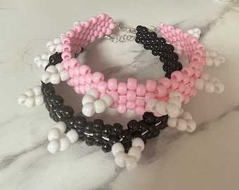 May include: Two beaded bracelets, one pink and white, the other black and white, with white star-shaped beads. The bracelets are connected by a silver chain.