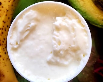 May include: A white plastic container filled with a thick, white cream. The cream has a smooth, whipped texture and is slightly textured.