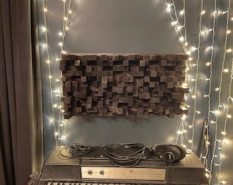 May include: A black sound-absorbing panel made of wood blocks, mounted on a wall with fairy lights. A black electric piano with a microphone and headphones sits in front of the panel.