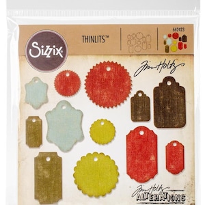 May include: A package of 12 die-cut metal craft dies for creating tags. The dies are in various shapes and sizes, including circles, stars, and rectangles. The dies are designed with a distressed, vintage look. The package includes the text "THINLITS™" and "Jim Holtz ALTERATIONS".