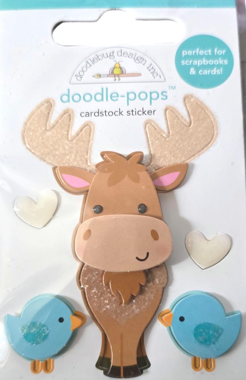 May include: Cardstock stickers featuring a moose, two blue birds, and two white hearts. The moose is brown with tan antlers and pink ears. The birds have orange beaks and feet. The stickers are perfect for scrapbooks and cards.