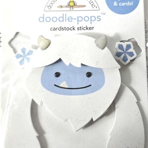 May include: A white cardstock sticker in the shape of a yeti with a light blue face and accents. The sticker is from Doodlebug Design Inc. and is labeled "doodle-pops" and "cardstock sticker". The packaging states it is perfect for scrapbooks and cards.