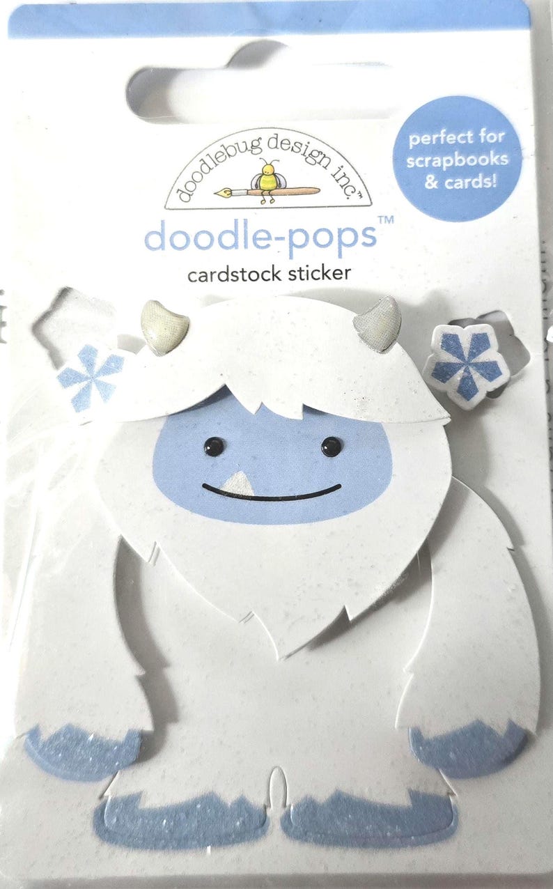 May include: A white cardstock sticker in the shape of a yeti with a light blue face and accents. The sticker is from Doodlebug Design Inc. and is labeled "doodle-pops" and "cardstock sticker". The packaging states it is perfect for scrapbooks and cards.