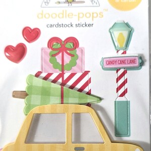 May include: Cardstock stickers featuring a yellow car, Christmas presents, a Christmas tree, and a street sign that reads "Candy Cane Lane." The stickers also include red hearts. The brand name is "doodle-pops".