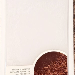 May include: A white 3D embossing folder with a poinsettia design. The folder is 5 inches by 7 inches (12.7 cm x 17.78 cm).