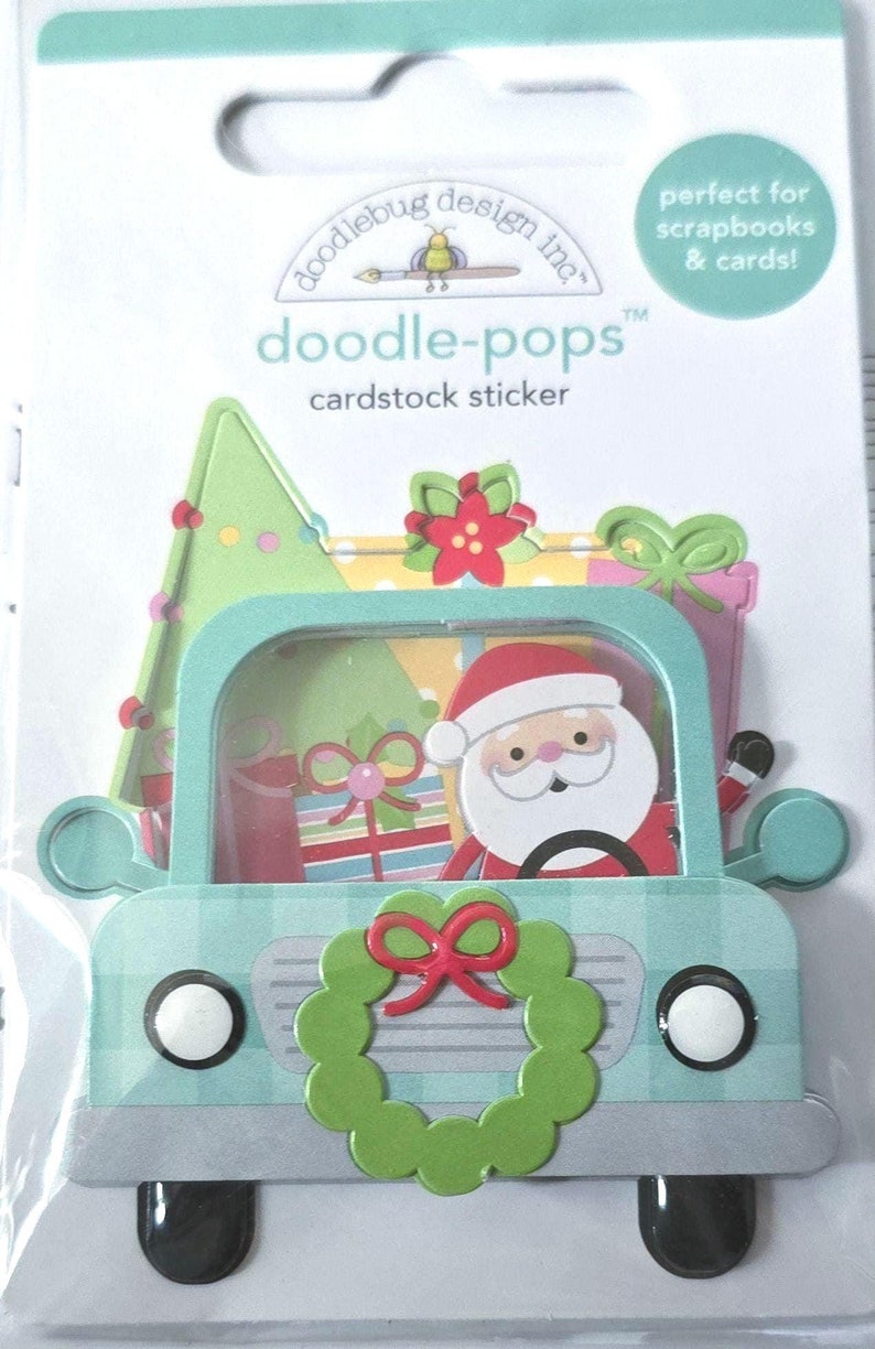 May include: A cardstock sticker featuring a teal truck with a Santa Claus driving. The truck bed is filled with gifts and a Christmas tree. A green wreath with a red bow adorns the front. The sticker is labeled "doodle-pops" and is perfect for scrapbooks and cards.