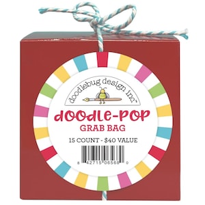 May include: A red square box with a colorful circular tag. The tag reads "doodle-POP GRAB BAG" with the "doodlebug design inc." logo. The tag has a colorful striped border. The box is tied with a blue and white string.