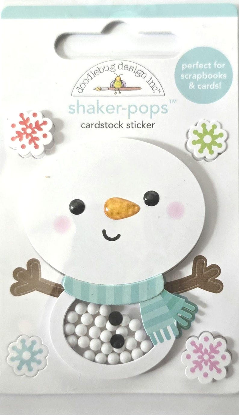 May include: A cardstock sticker featuring a snowman design with a shaker element. The snowman has a carrot nose, black eyes, and a blue scarf. The package includes snowflake stickers and text that reads "shaker-pops" and "perfect for scrapbooks & cards!"