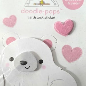 May include: A cardstock sticker set featuring a white polar bear and pink hearts. The sticker set includes the text "doodle-pops" and "cardstock sticker". The packaging also includes the text "perfect for scrapbooks & cards!"