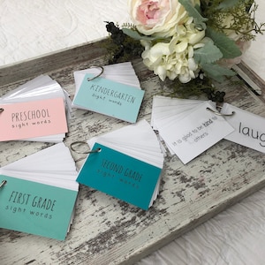 May include: A set of five ring-bound flashcard sets for different grade levels. The cards are labelled "Preschool sight words", "Kindergarten sight words", "First Grade sight words", "Second Grade sight words", and "It is good to be kind to others". There is also a single flashcard with the word "laugh" on it.