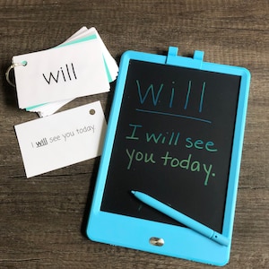 May include: A blue LCD writing tablet with a stylus. The tablet has a black screen with the words "Will I will see you today." written on it. There are also two white index cards with the word "will" written on them.