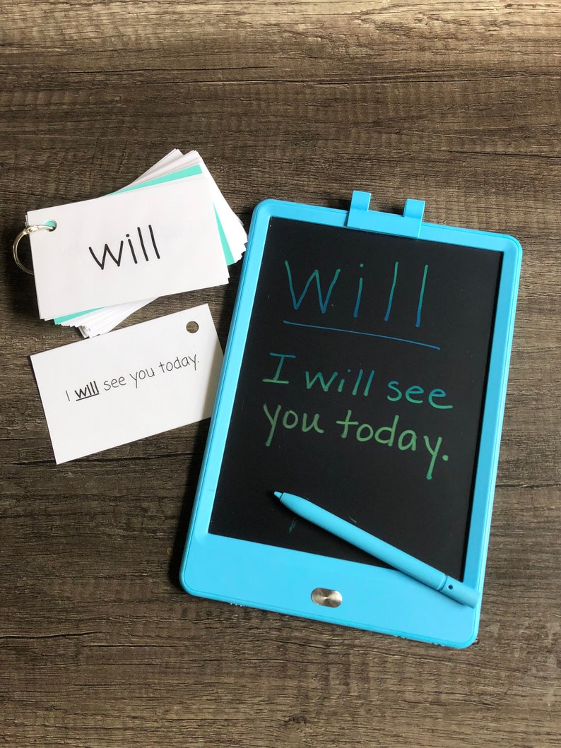 May include: A blue LCD writing tablet with a stylus. The tablet has a black screen with the words "Will I will see you today." written on it. There are also two white index cards with the word "will" written on them.