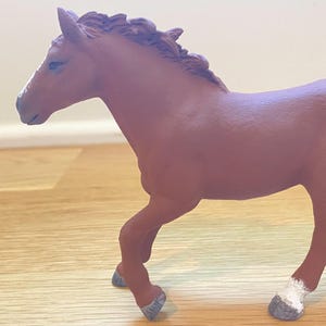 May include: A brown toy horse figurine with a white blaze on its face and white markings on its hooves. The horse is posed mid-stride, with its legs in motion. The figurine is made of a solid material.