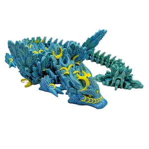 Puede incluir: Figura articulada de dragón en tonos turquesa y verde azulado, con detalles amarillos. El dragón presenta una textura detallada, similar a escamas, una cola segmentada y detalles intrincados.