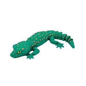 Peut inclure: Un lézard jouet vert avec des taches orange et des yeux jaunes. Le lézard est allongé sur un fond blanc. La queue est segmentée et incurvée. Le lézard a quatre pattes avec des pieds détaillés.