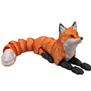 May include: An articulated fox figurine featuring a vibrant orange body with a white chest and tail tip. The fox has black ears, black legs, and blue eyes. The body is constructed from multiple segmented pieces that allow for flexible movement.