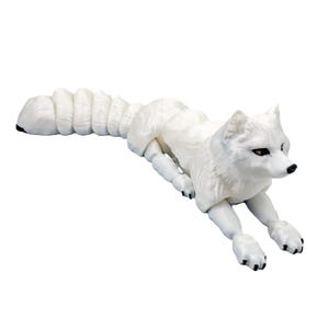 Könnte beinhalten: Eine weiße Polarfuchsfigur mit einem langen, flauschigen Schwanz und schwarzen Pfoten. Der Fuchs liegt in einer liegenden Pose, mit ausgestreckten Vorderbeinen. Die Figur hat eine detaillierte Fellstruktur und dunkle Augen.