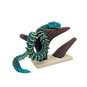 May include: A turquoise and yellow snake figurine coiled around a brown wooden structure. The snake has a detailed scale pattern and a small, round head. The base is a light beige colour.