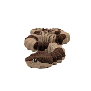 Puede incluir: Escultura artesanal en forma de serpiente, marrón y beige, con escamas detalladas y ojos realistas. La serpiente está enrollada, con la cabeza levantada, mostrando su intrincado diseño. Ideal para la decoración del hogar o como regalo original.