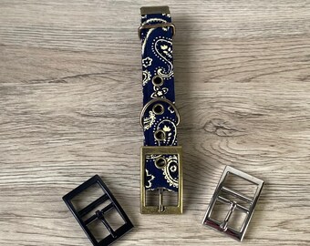 Könnte beinhalten: Ein marineblaues Hundehalsband mit weißem Paisley-Muster, das drei verschiedene Hardware-Farboptionen zeigt: Schwarz, Messing und Silber. Das Halsband wird auf einer Holzoberfläche präsentiert, mit dem Text "3 different hardware colours" oben.