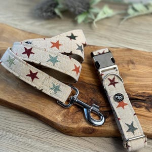 May include: A beige dog collar and lead set with a multi-coloured star pattern. The collar has a silver buckle and the lead has a silver hook.