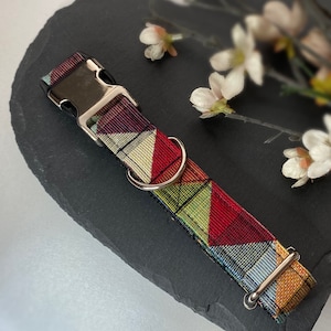 May include: A colorful dog collar with a geometric pattern in red, green, yellow, and blue. The collar has a silver metal buckle and a matching D-ring for leash attachment. The collar is made of a durable fabric.