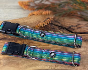 May include: Two dog collars with a vibrant striped design in blue, green, pink, and yellow. Each collar features a black plastic buckle and a silver metal D-ring. The collars are displayed on a wooden surface.