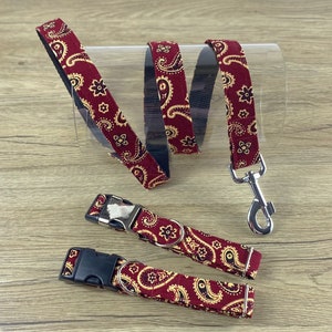 May include: A burgundy paisley dog collar and lead set. The set includes two collars, one with a metal buckle and one with a plastic buckle, and a matching lead with a metal clasp. The paisley pattern is gold on a burgundy background.