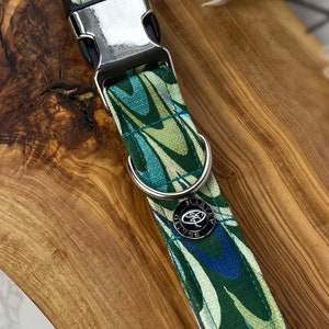 May include: A green, blue and white patterned dog collar with a silver buckle and a silver ring. The collar has a silver tag with the text "Harvey Oliver" on it.