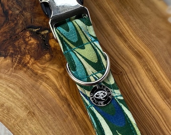 May include: A green, blue and white patterned dog collar with a silver buckle and a silver ring. The collar has a silver tag with the text "Harvey Oliver" on it.