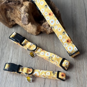 Peut inclure: Colliers pour chiens jaunes avec un motif de marguerites et d'abeilles. Les colliers ont des boucles en plastique noir et un anneau en D en métal. Chaque collier a un petit charme d'abeille. Sur une surface en bois.