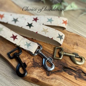 Pu&ograve; includere: Scelta di ferramenta per un guinzaglio per cani. Il guinzaglio &egrave; realizzato in tessuto color crema con stelle multicolori. Le opzioni di ferramenta includono nero, argento e ottone anticato.