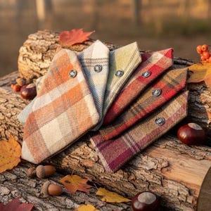 Op de afbeelding: Een collectie van zes driehoekige huisdierbandana's gemaakt van wolachtige ruitstof in diverse herfstkleuren zoals oranje, crème, groen, rood en bruin. Elke bandana is voorzien van een zilverkleurige metalen knoop met een cirkelvormig reliëf.