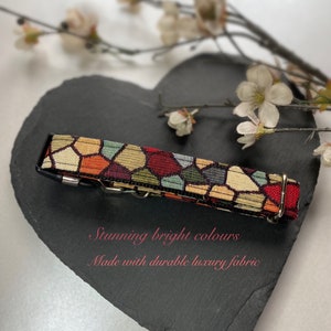 Könnte beinhalten: Ein farbenfrohes Hundehalsband mit einem geometrischen Muster in Rot, Gold, Grün und Orange. Es hat eine Metallschnalle und eine schwarze Rückseite. Der Text auf dem Bild lautet "Stunning bright colours" und "Made with durable luxury fabric."