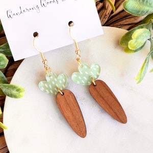 May include: A pair of wooden carrot earrings with green and white polka dot tops. The earrings are on a white card with the text "Wandering Woods Designs".