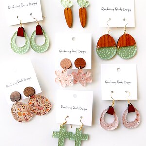 May include: Assortment of handmade acrylic earrings with various designs, including floral, bunny, carrot, cross, and geometric shapes. The earrings are all in shades of green, pink, and brown.