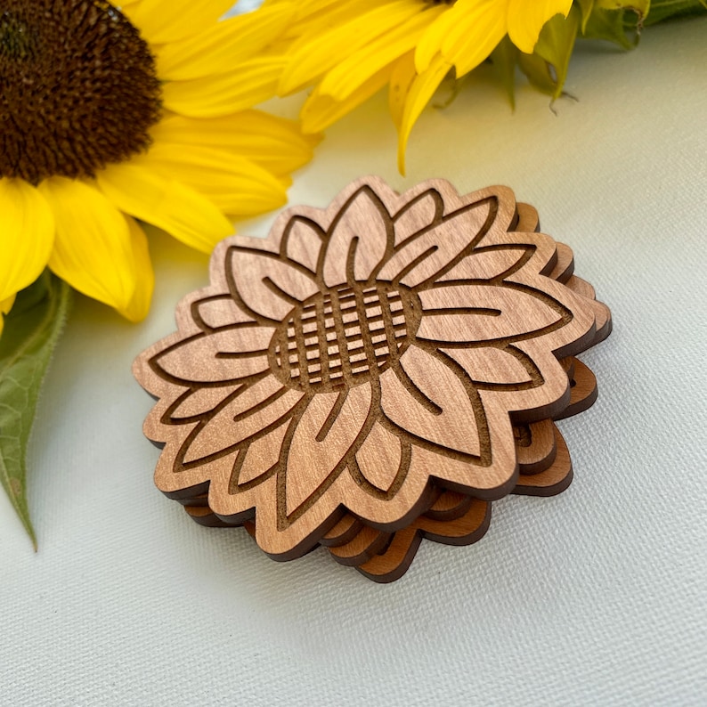 May include: Set of four wooden coasters featuring a sunflower design. The coasters are made of natural wood and have a light brown color.
