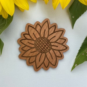 May include: A wooden cutout of a sunflower with a brown wood grain finish. The sunflower is outlined in a darker brown color.