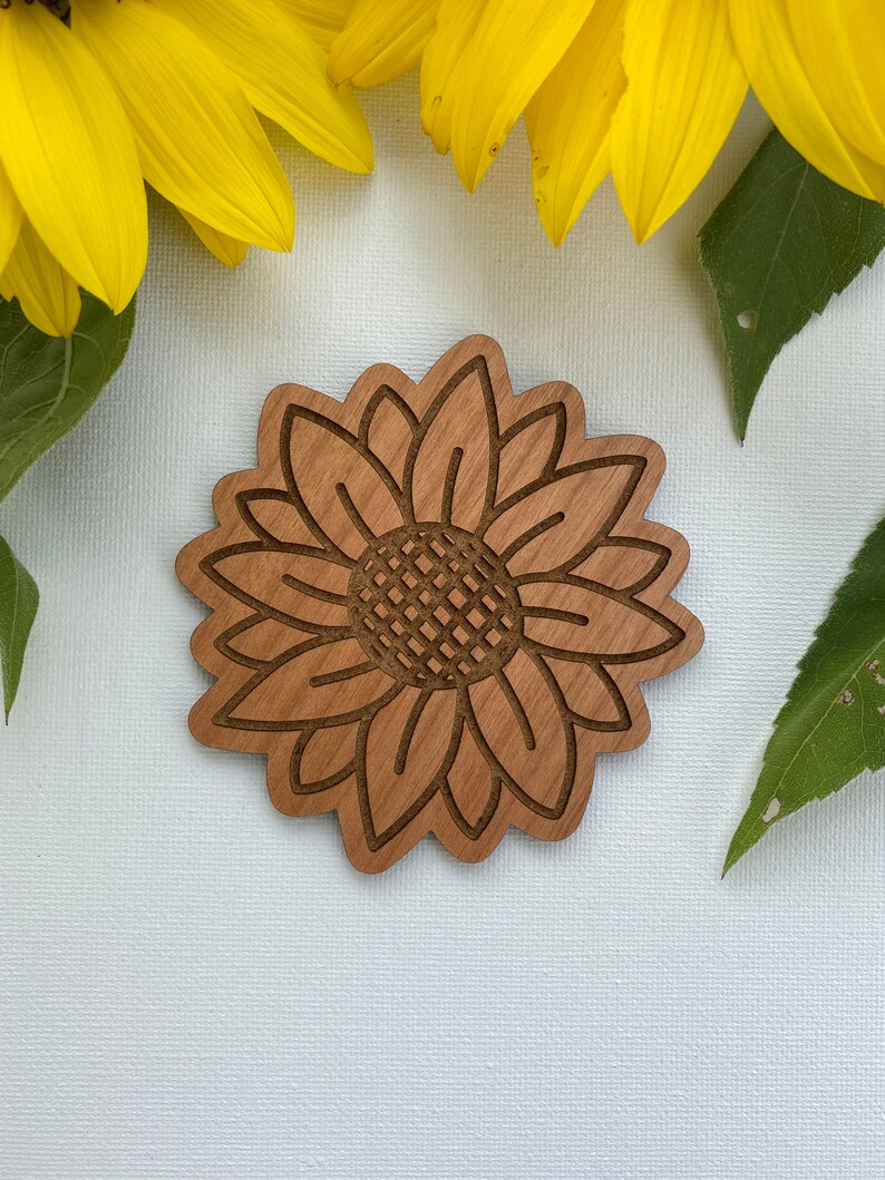 May include: A wooden cutout of a sunflower with a brown wood grain finish. The sunflower is outlined in a darker brown color.