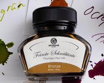May include: Three glass bottles of Octopus Fluids fountain pen ink with black caps, labeled "Linagrun", "Bronze", and "Purpur". Ink splotches in green, brown, and purple are on white paper. The Octopus logo is visible.