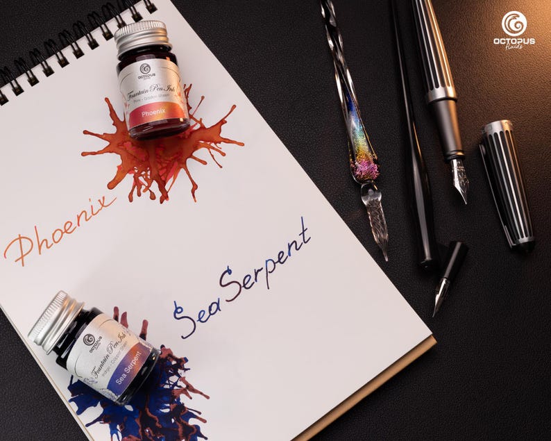 Pu&ograve; includere: Due flaconi di inchiostro, uno rosso e uno blu, con i nomi "Phoenix" e "Sea Serpent" scritti su un taccuino bianco. I flaconi sono etichettati "Fountain Pen Ink".