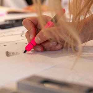 Puede incluir: Una mano sosteniendo un rotulador rosa y dibujando sobre una superficie blanca. La persona lleva una pulsera dorada en la mu&ntilde;eca.