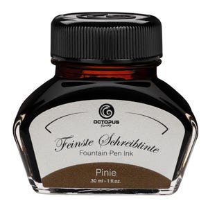 Op de afbeelding: Een heldere glazen fles bruine inkt voor vulpennen met een zwarte dop. Het etiket leest "Feinste Schreibtinte" en "Pinie". De fles bevat 30 ml inkt.