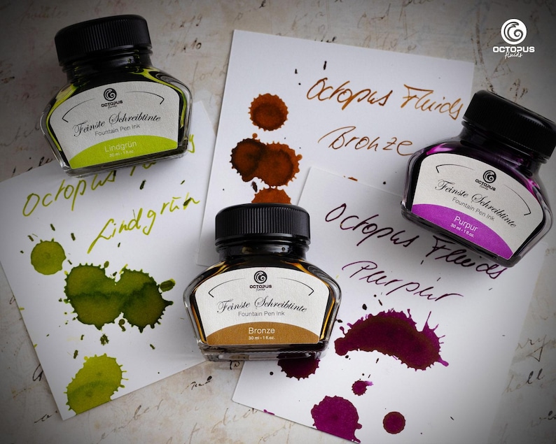 May include: Three glass bottles of Octopus Fluids fountain pen ink with black caps, labeled "Linagrun", "Bronze", and "Purpur". Ink splotches in green, brown, and purple are on white paper. The Octopus logo is visible.
